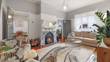 A cozy living room with a fireplace, a sofa, a coffee table, and a dining area with chairs.