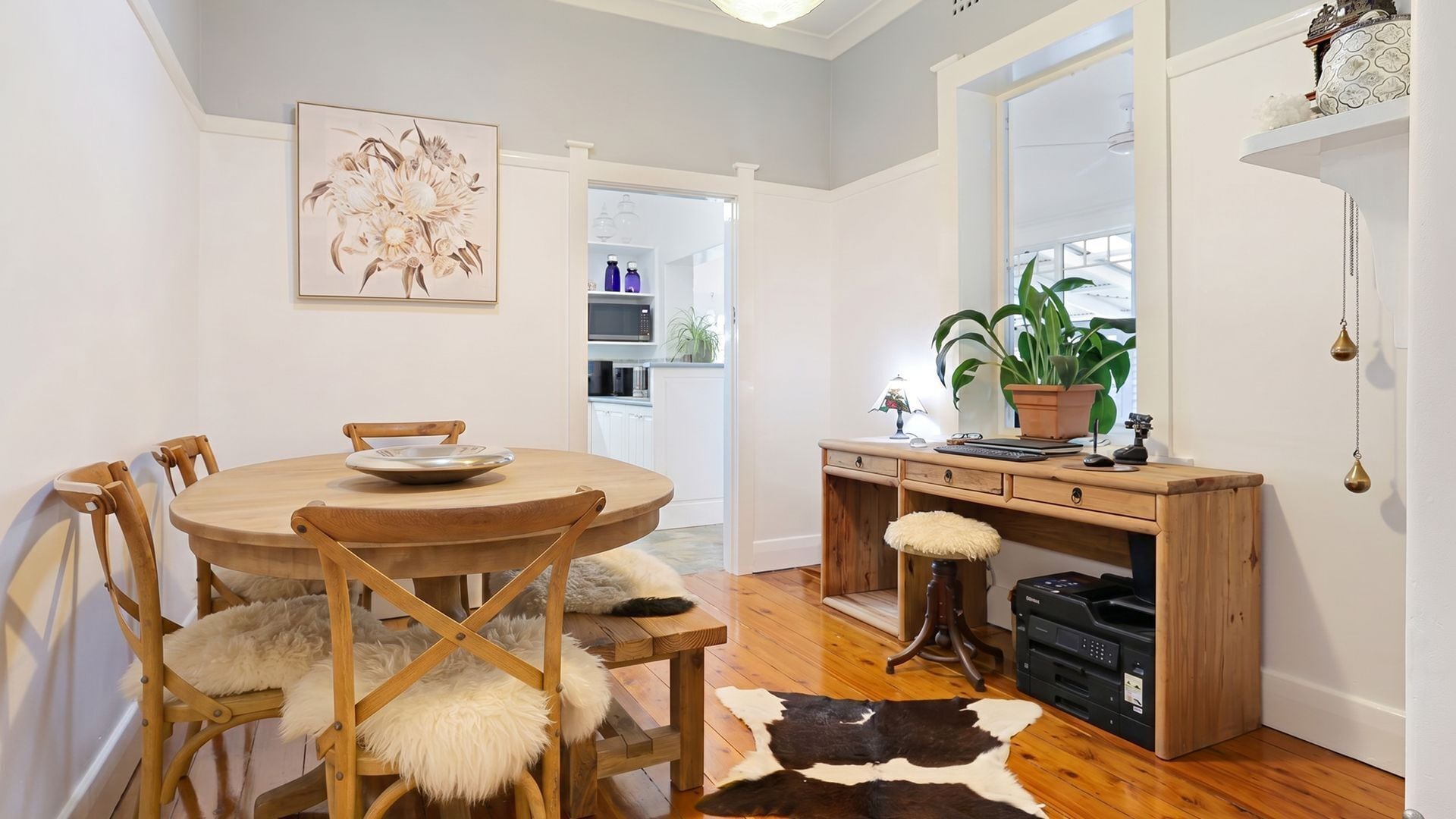 A dining area with a round table, chairs, a cowhide rug, a desk with a computer, and a potted plant.
