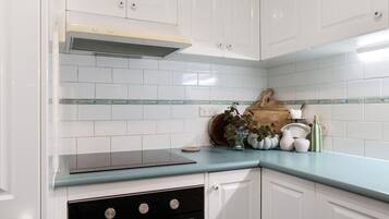 A kitchen with white cabinets, a blue countertop, a stove, and a vent hood.
