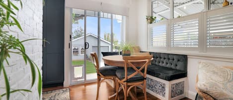 A room with a round table, two chairs, a dark sofa, a window with blinds, and a door leading outside.
