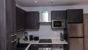 A modern kitchen with dark wood cabinets, a stainless steel microwave, a built-in oven, a coffee maker, and a toaster. - Loxwood Executive 1BR | Airport City • Pool • Gym (Accra)