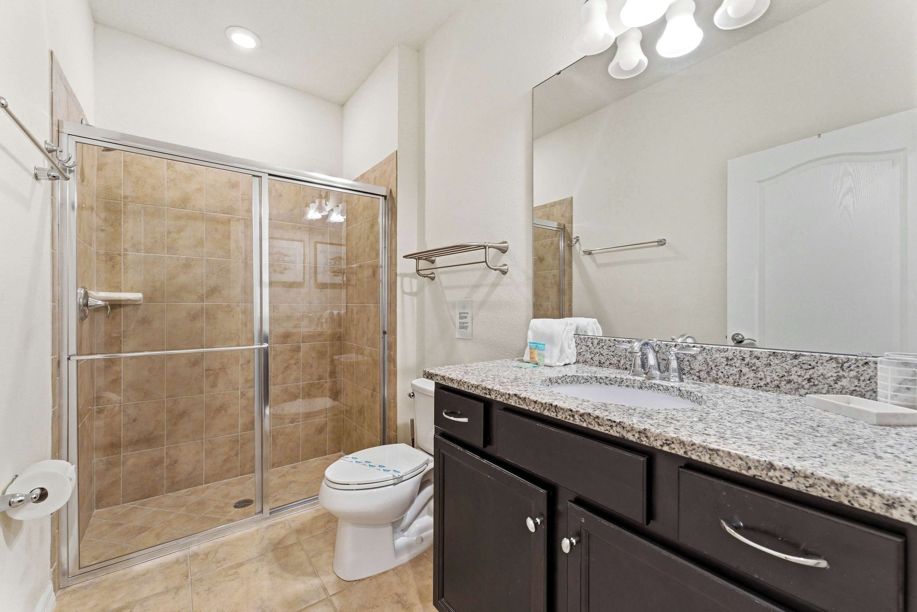 A bathroom with a shower, toilet, sink, and dark cabinets.