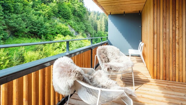Un balcon avec deux chaises blanches et une terrasse en bois donnant sur une zone boisée.