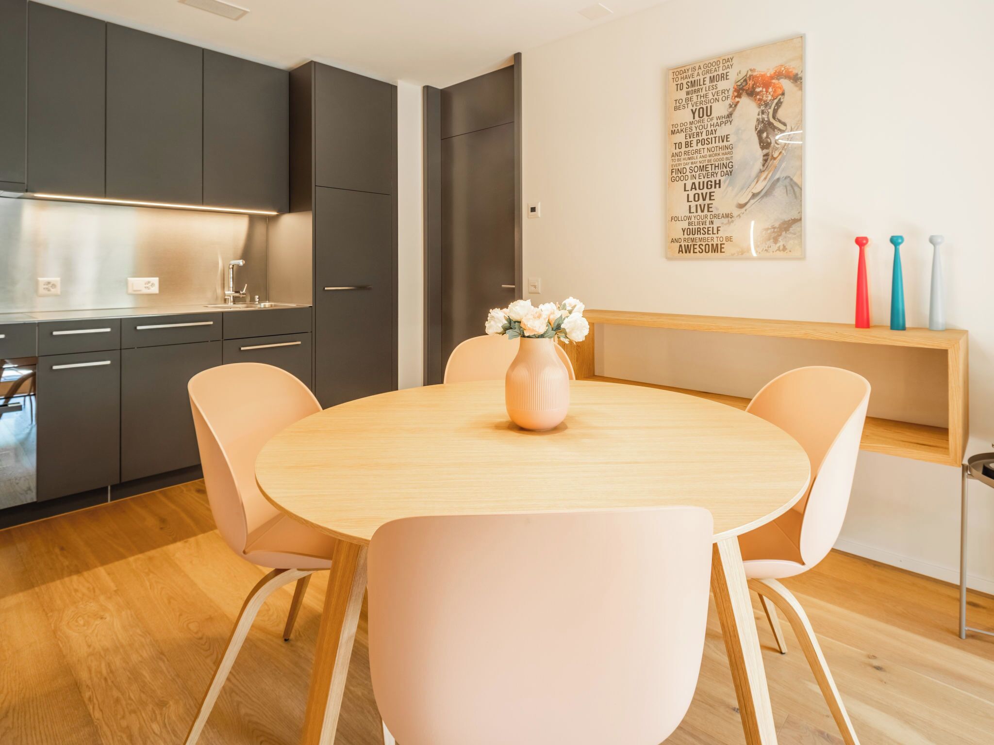 Een moderne keuken met donkere kastjes, een houten eettafel en stoelen.