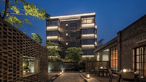 A courtyard with outdoor seating, a stone wall, and a building with multiple floors and balconies. - Sail Hotel (Chongqing)
