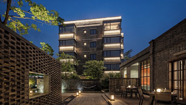 A courtyard with outdoor seating, a stone wall, and a building with multiple floors and balconies. - Sail Hotel (Chongqing)