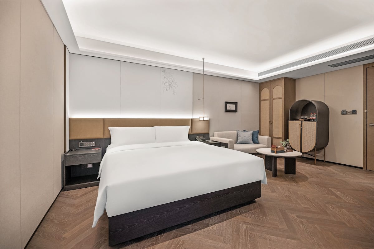 A modern hotel room with a large bed, a bedside table, a nightstand, a sofa, a small table, and a wardrobe.