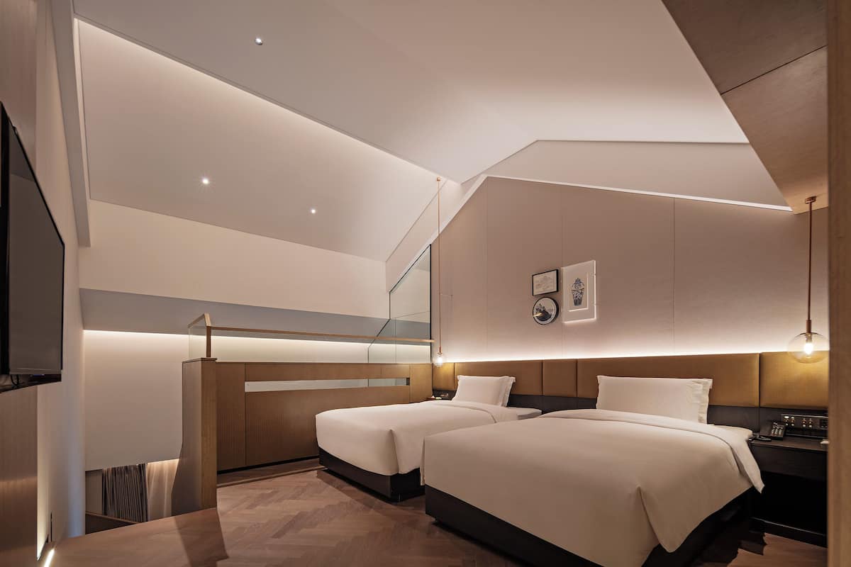A modern hotel room with two beds, a desk, and a large window.