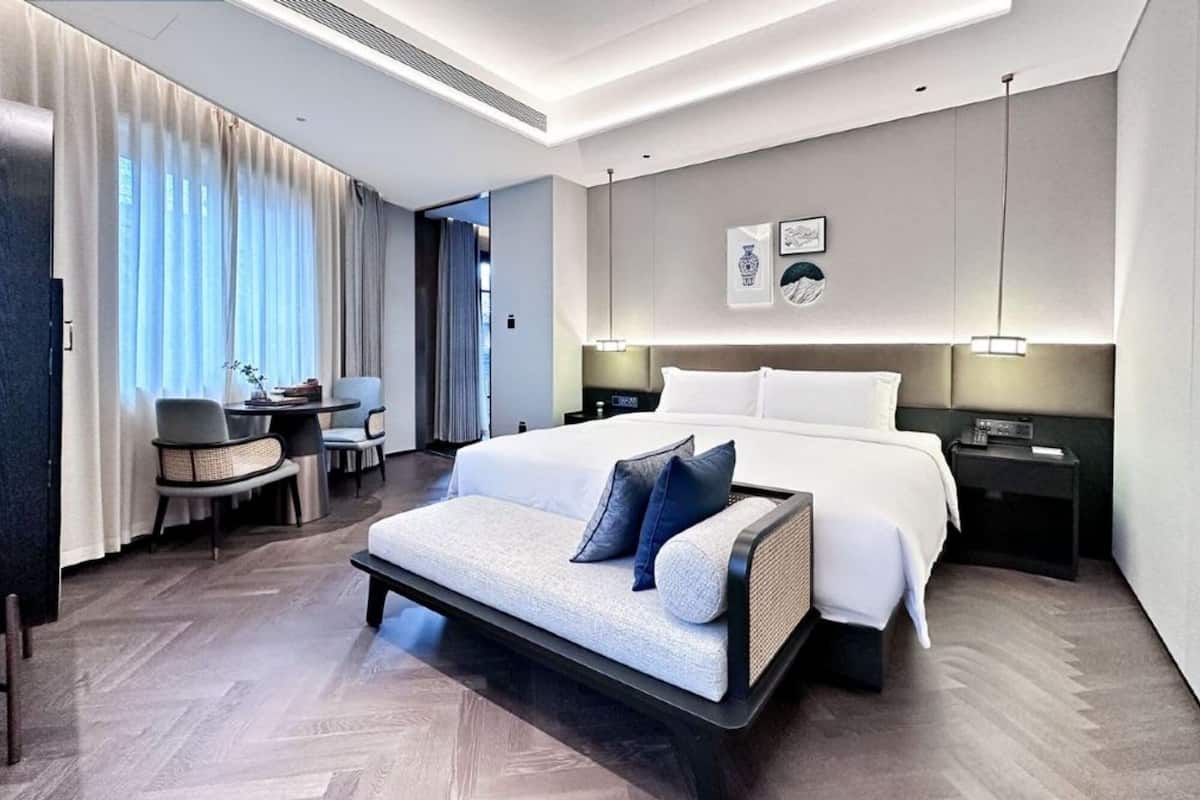 A modern hotel room with a large bed, a sofa, a desk, and a chair.
