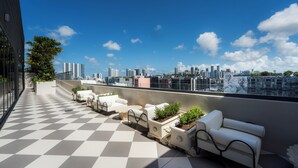 Une terrasse sur le toit avec un sol à carreaux, des meubles d’extérieur blancs et une vue panoramique sur la ville.