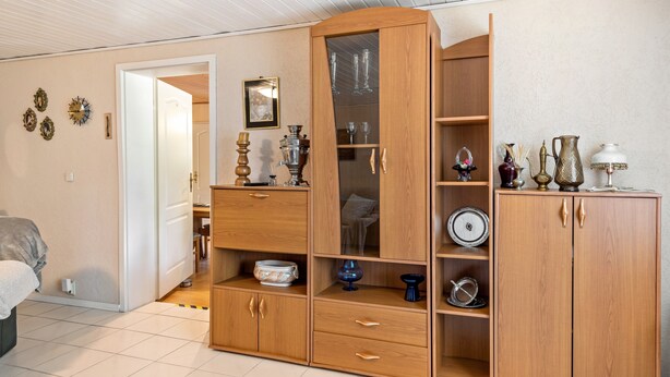 Ein Zimmer mit Holzschrank, Bett und einer Tür zu einem anderen Raum, sowie einer Wand mit Dekorationen.