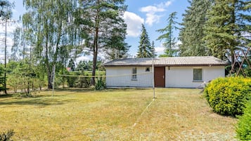 Ein eingeschossiges Haus mit Ziegeldach, umgeben von einer grünen Wiese und dichten Bäumen.