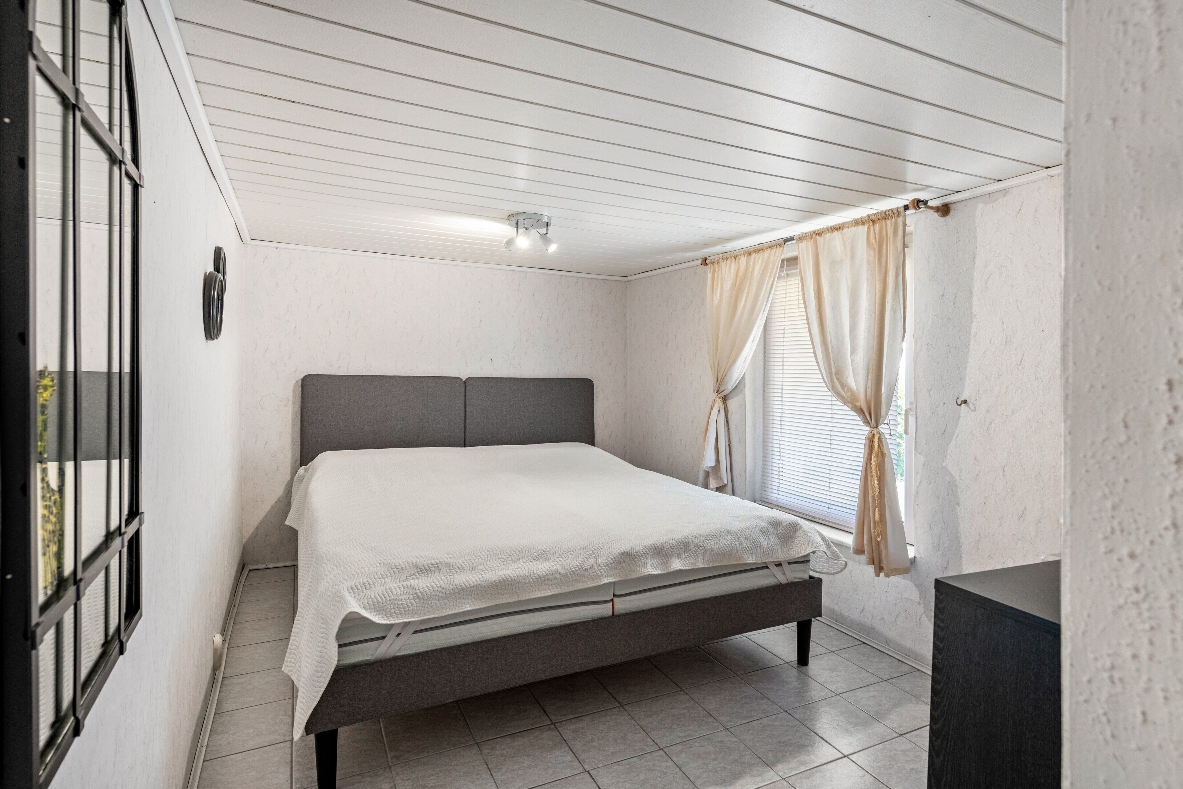 A bedroom with a bed, a window with curtains, and a ceiling fan.