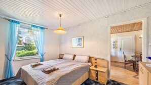 Ein Schlafzimmer mit Bett, Nachttisch, Lampe und Blick auf einen Essbereich.