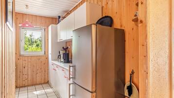 A compact kitchen with wooden walls, a white countertop, and a stainless steel refrigerator.