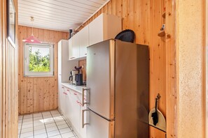 Una cocina compacta con paredes de madera, una encimera blanca y un refrigerador de acero inoxidable.
