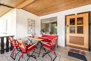 Un área de estar al aire libre techada, con una mesa de madera y cuatro sillas rojas con cojines.