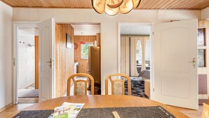 Ein Zimmer mit Holzboden, einem Esstisch mit Stühlen, einem durchgehenden Durchgang zur Küche und einem Bett im angrenzenden Raum.