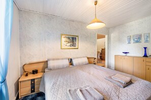 Un dormitorio con cama, mesita de noche, lámpara y un cuadro en la pared.