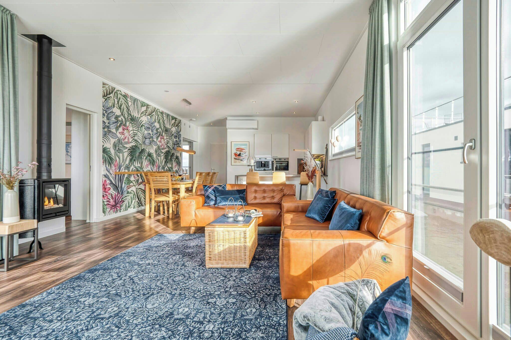 Un salon moderne avec un canapé, une table basse et une cheminée. On y trouve également un coin repas avec des chaises et une table, ainsi qu’une cuisine à l’arrière-plan.