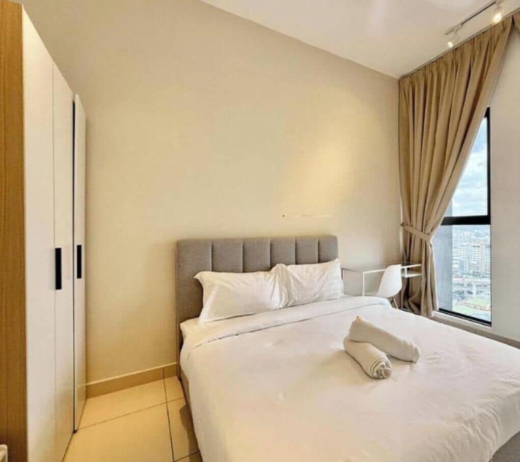 A hotel room with a bed, a nightstand, a window with curtains, and a view of the city.
