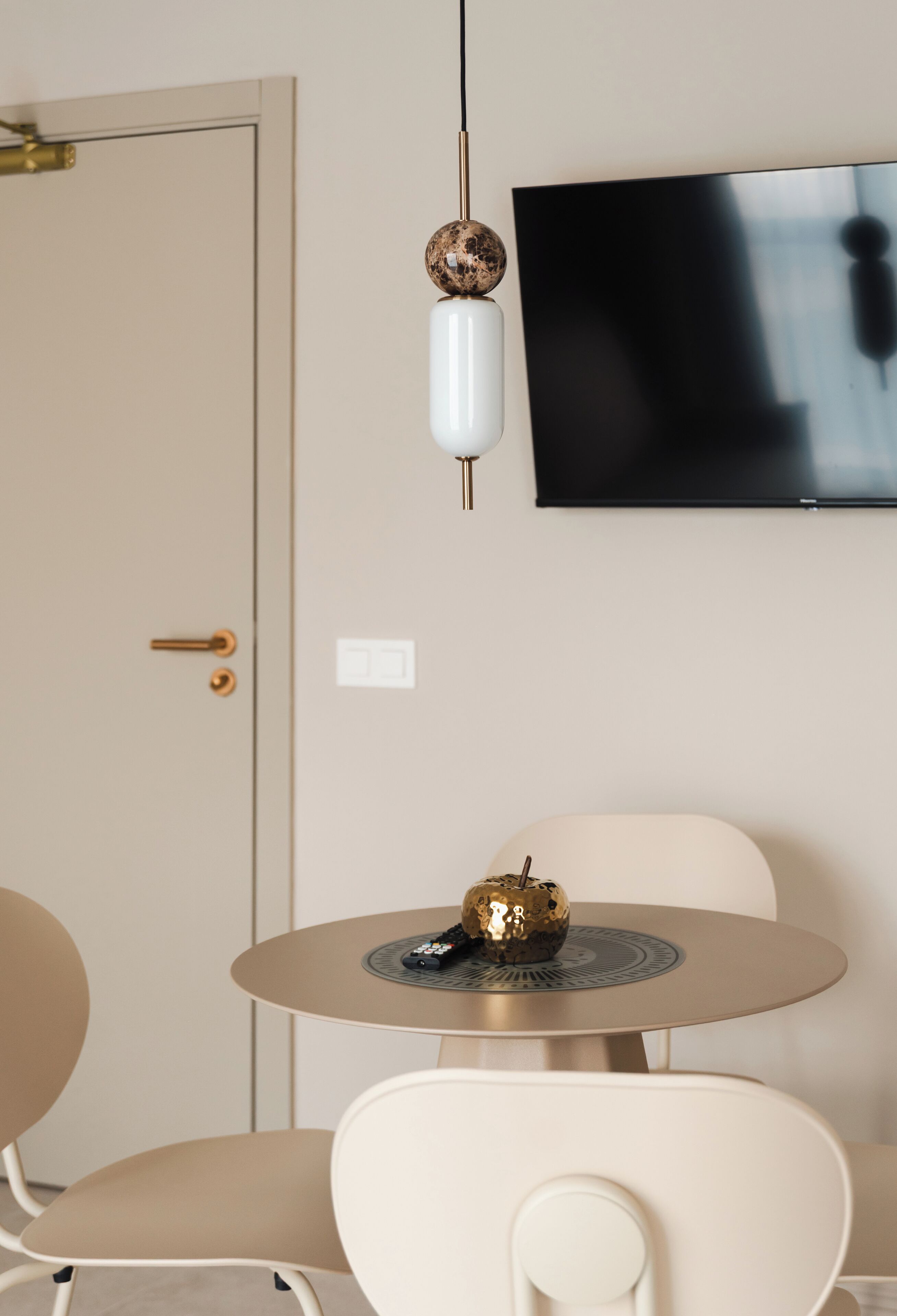 Een kamer met een deur, een ronde tafel met stoelen, een aan de muur bevestigde televisie, en een decoratieve bol op de tafel.