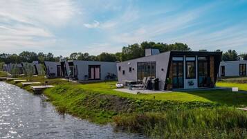 A modern outdoor setting with a river, a grassy area, and a building with large windows and a patio.