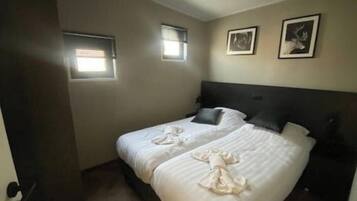 A bedroom with a bed, two windows, and two framed pictures on the wall.