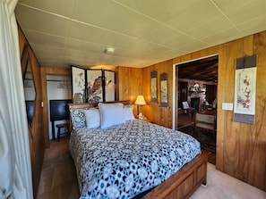 A bedroom with a bed, bedside table, lamp, and wooden paneling. - The Pilot House at Point Bailly (Pacific Beach)