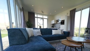 A modern living room with a sectional sofa, a coffee table, and a view of the kitchen and outdoors. - Holiday Home in Hindeloopen With Wi-fi (Hindeloopen)