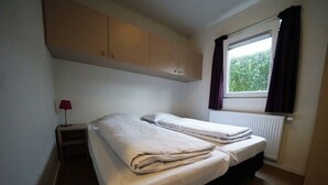 Une petite chambre avec un lit simple, une fenêtre, un radiateur et un bureau avec une lampe.