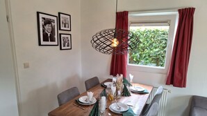 Un coin repas avec une table en bois, des chaises grises, un luminaire suspendu et une fenêtre ornée de rideaux rouges.