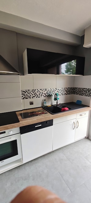 A modern kitchen with white cabinets, a black countertop, a tiled backsplash, and a window above the sink. - Vrbo Property (Mulhouse)