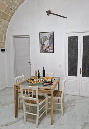 Ein Essbereich mit Marmorboden, einem Holztisch mit weißen Stühlen, einem gerahmten Bild an der Wand und einer Tür mit satinierten Glasscheiben.