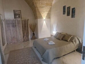 A bedroom with a bed, a nightstand, a lamp, a painting, and a stone wall. - Puglia vacation, entire house near Gallipoli (Parabita)