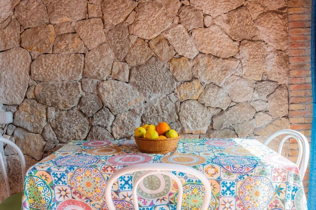 Un muro de piedra, una mesa con mantel colorido y una cesta de fruta.