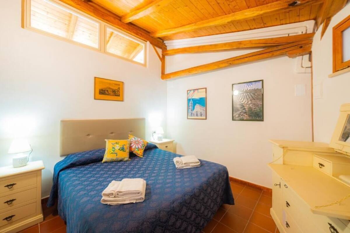 A bedroom with a bed, a nightstand, a dresser, and a ceiling with wooden beams.