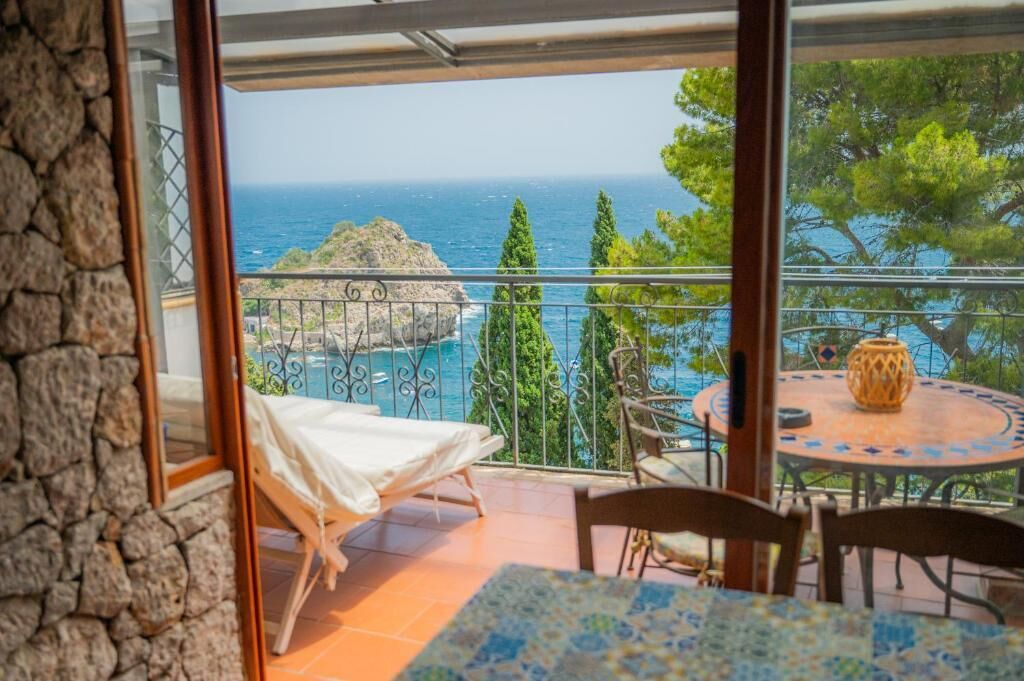 Ein Balkon mit Bett, Tisch und Stühlen, mit Blick auf die Küste, Bäume und eine Felsformation.