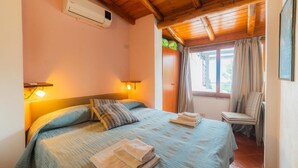 Un dormitorio con una cama, dos lámparas de noche, una ventana con cortinas, una silla y un equipo de aire acondicionado.