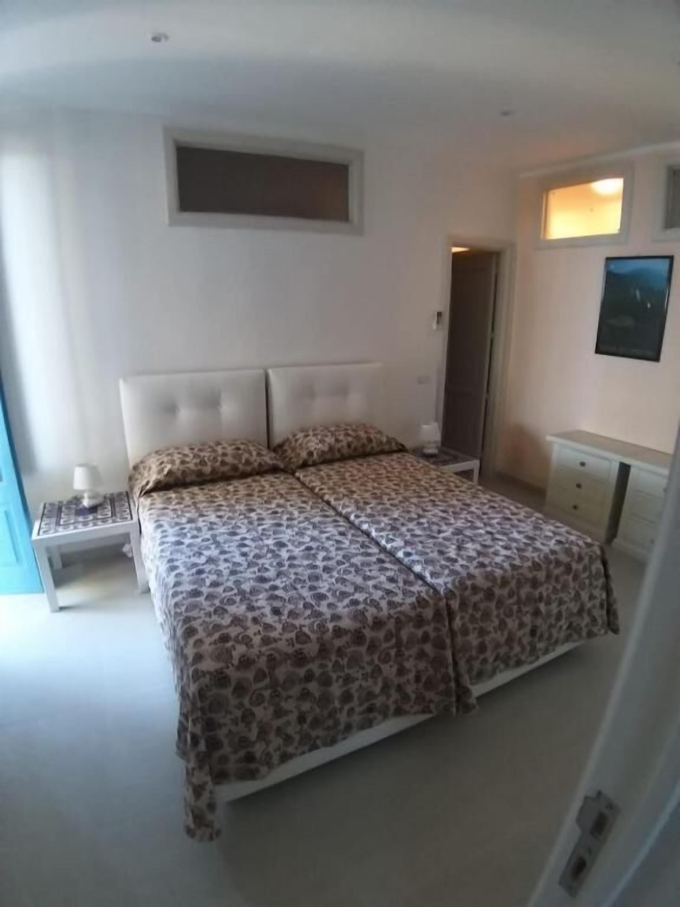 A bedroom with a bed, a nightstand, a dresser, and a small window.