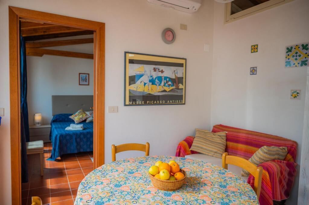 A room with a bed, a table with a basket of fruit, a sofa, and a wall with a framed picture.