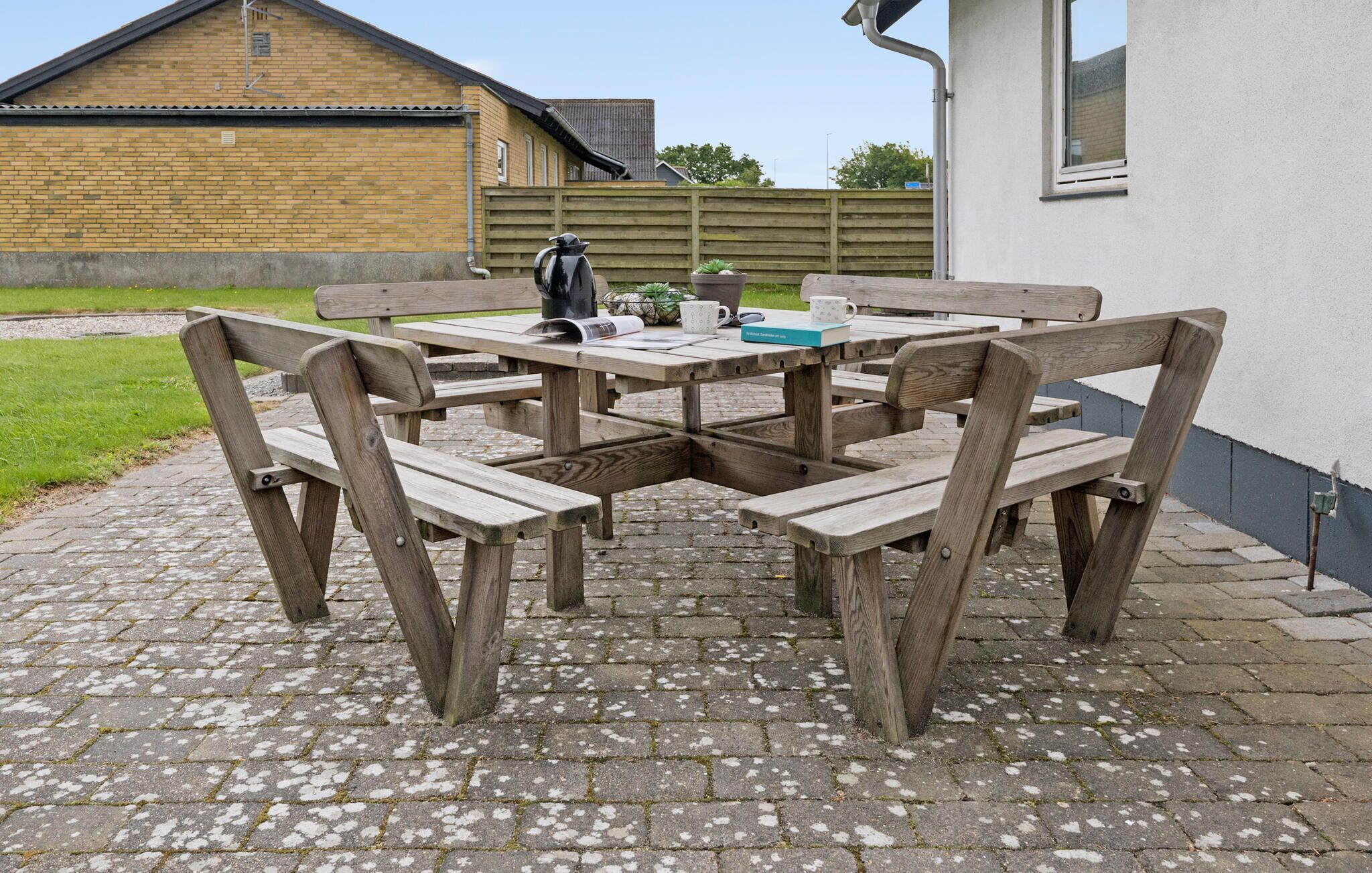 Une table de pique-nique en bois, avec des bancs, sur une terrasse dallée.