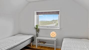 Una habitación pequeña con dos camas, una ventana que da a la vista de una carretera y colinas, una mesita con una revista y una planta.