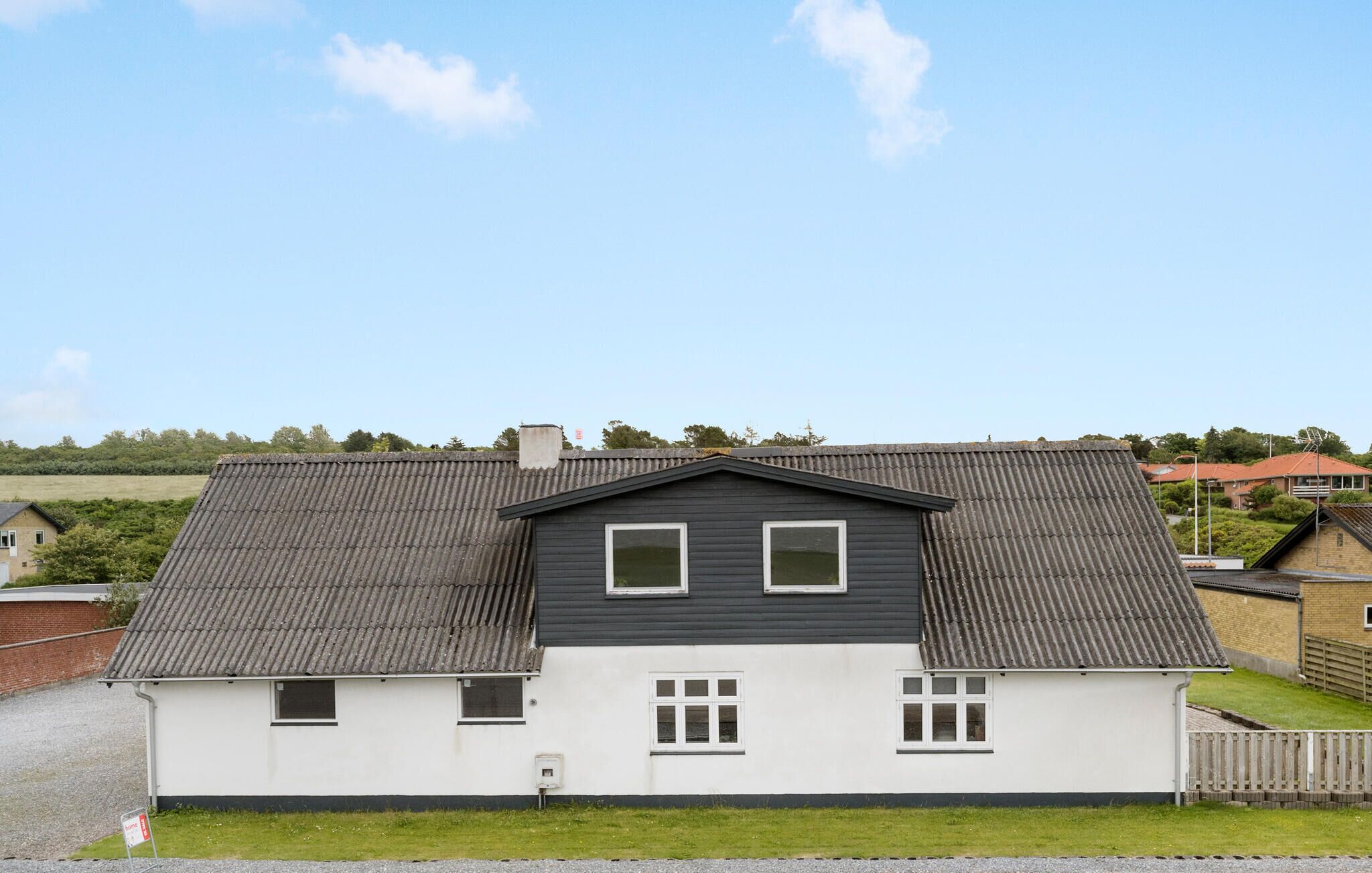 Une maison à deux étages, avec un toit gris et des murs blancs, dotée de deux fenêtres à l’étage supérieur et de trois au rez-de-chaussée.