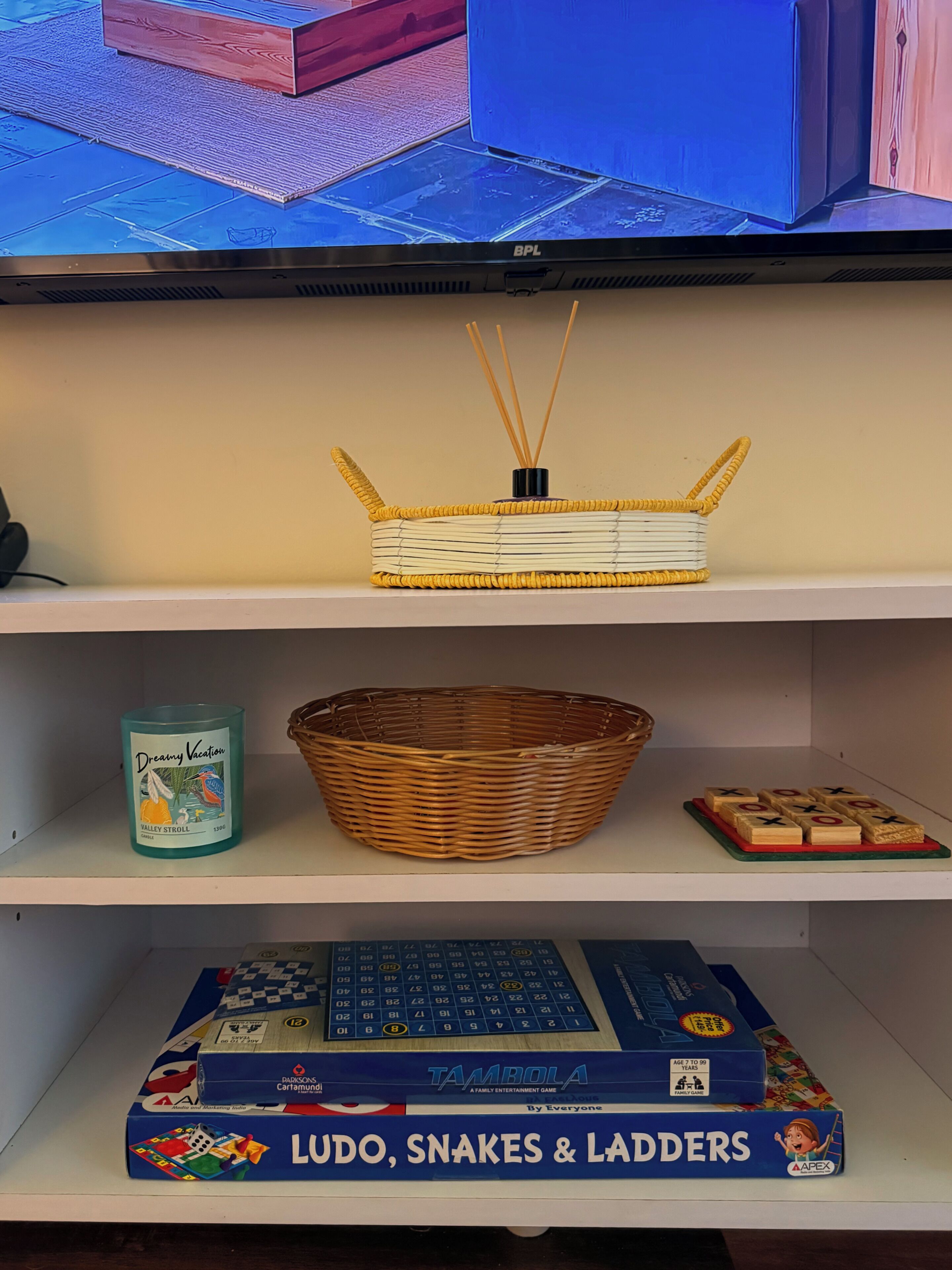 Una estantería con una cesta tejida, una vela perfumada y un juego de mesa.