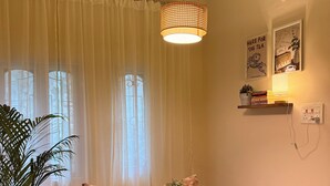 Una habitación acogedora con una mesa redonda de madera, dos sillas, un pequeño banco, una planta en maceta y una lámpara colgante.