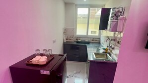 A compact kitchen with a refrigerator, a sink, and a window. - Cabana Suites (Rishikesh)
