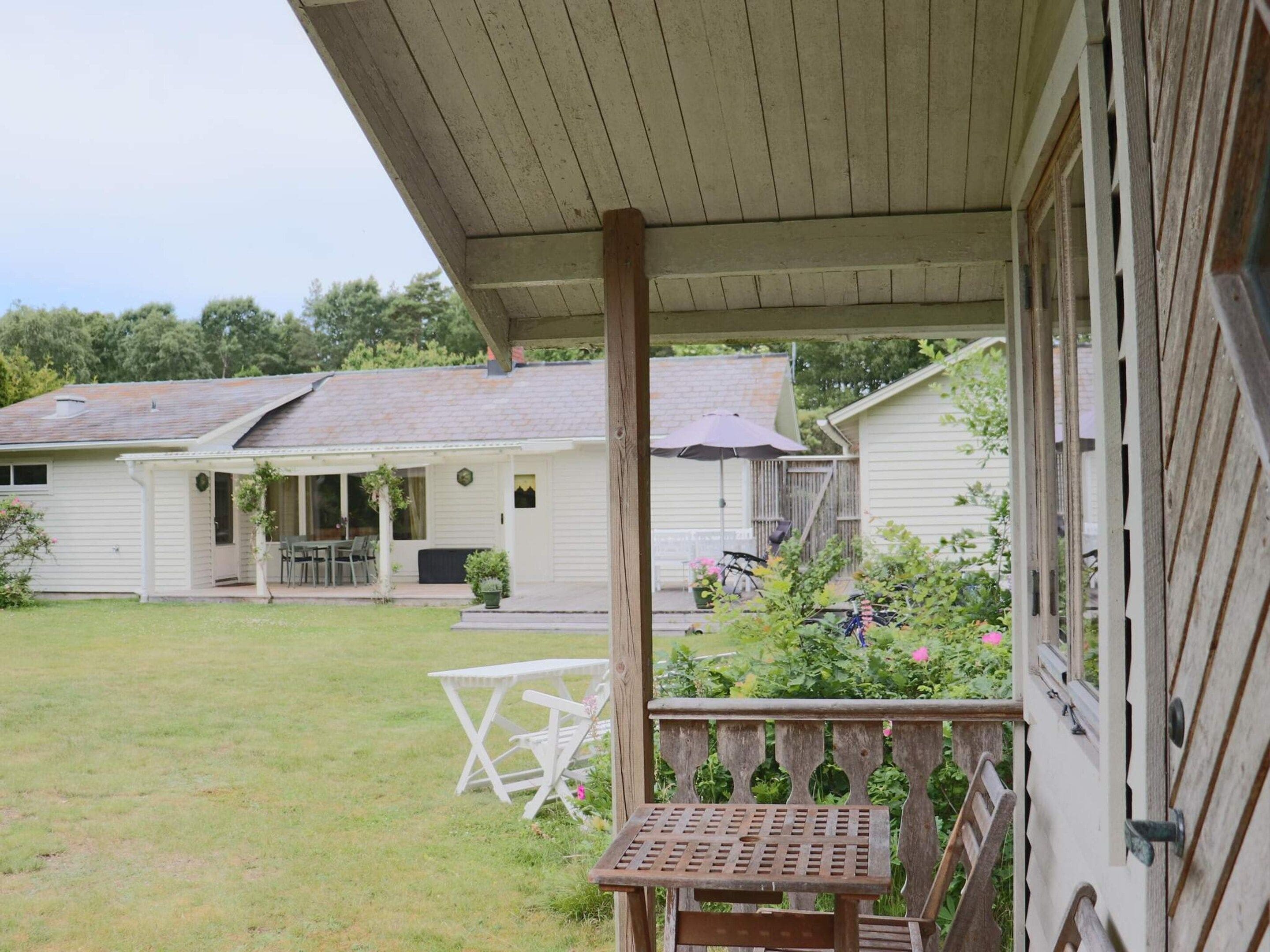 A covered porch with a wooden bench, a small table, and a white folding chair.