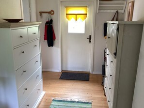A narrow hallway with a wooden floor, a white door with a window, and a coat rack with two jackets. - 4 Star Holiday Home in Heberg (Heberg)