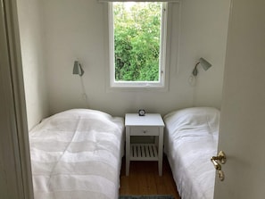 Ein kleines Schlafzimmer mit einem Bett, einem Fenster, einem Nachttisch und einer abschließbaren Tür.
